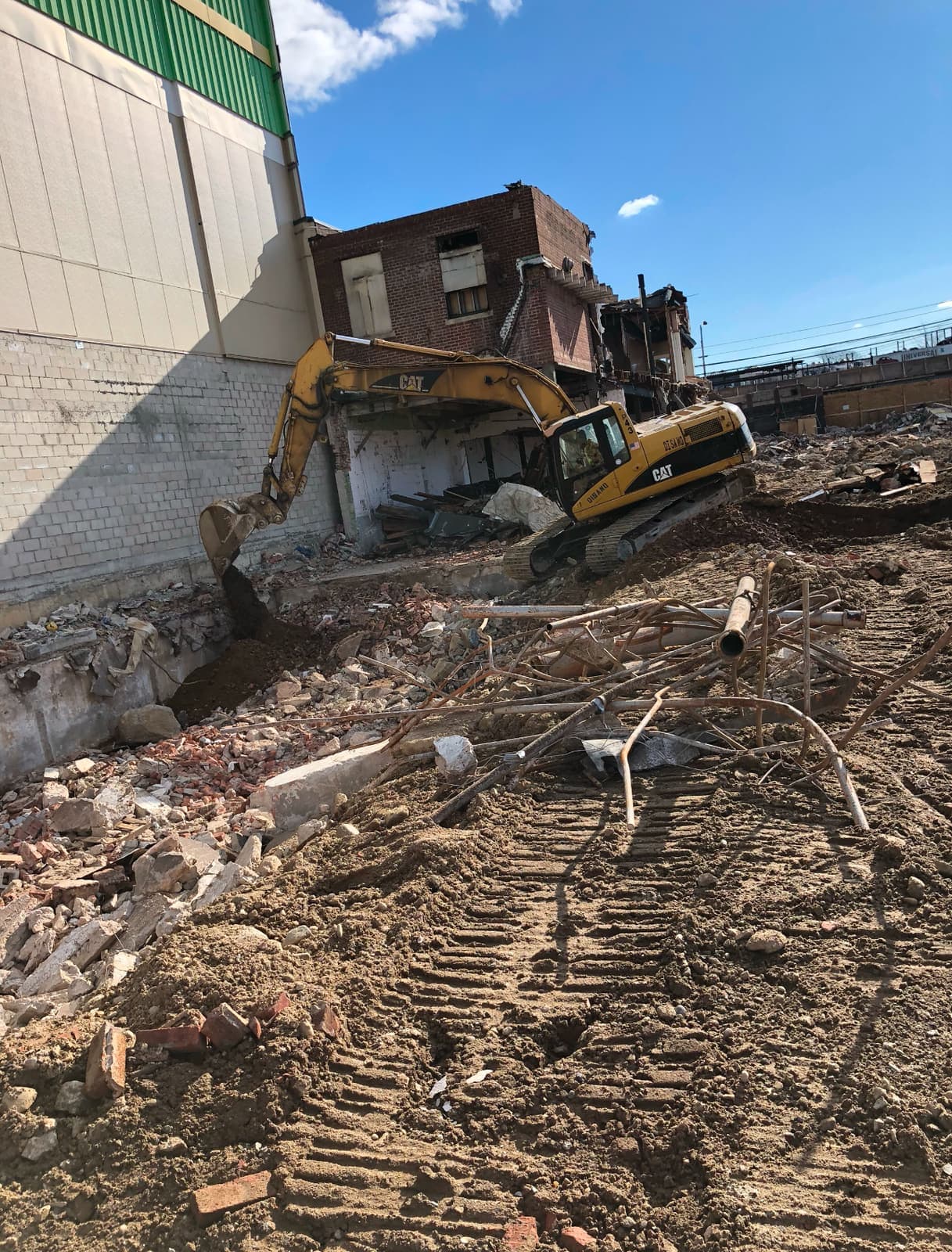 An excavator tearing down a brick building, with demolition debris spread across the site.