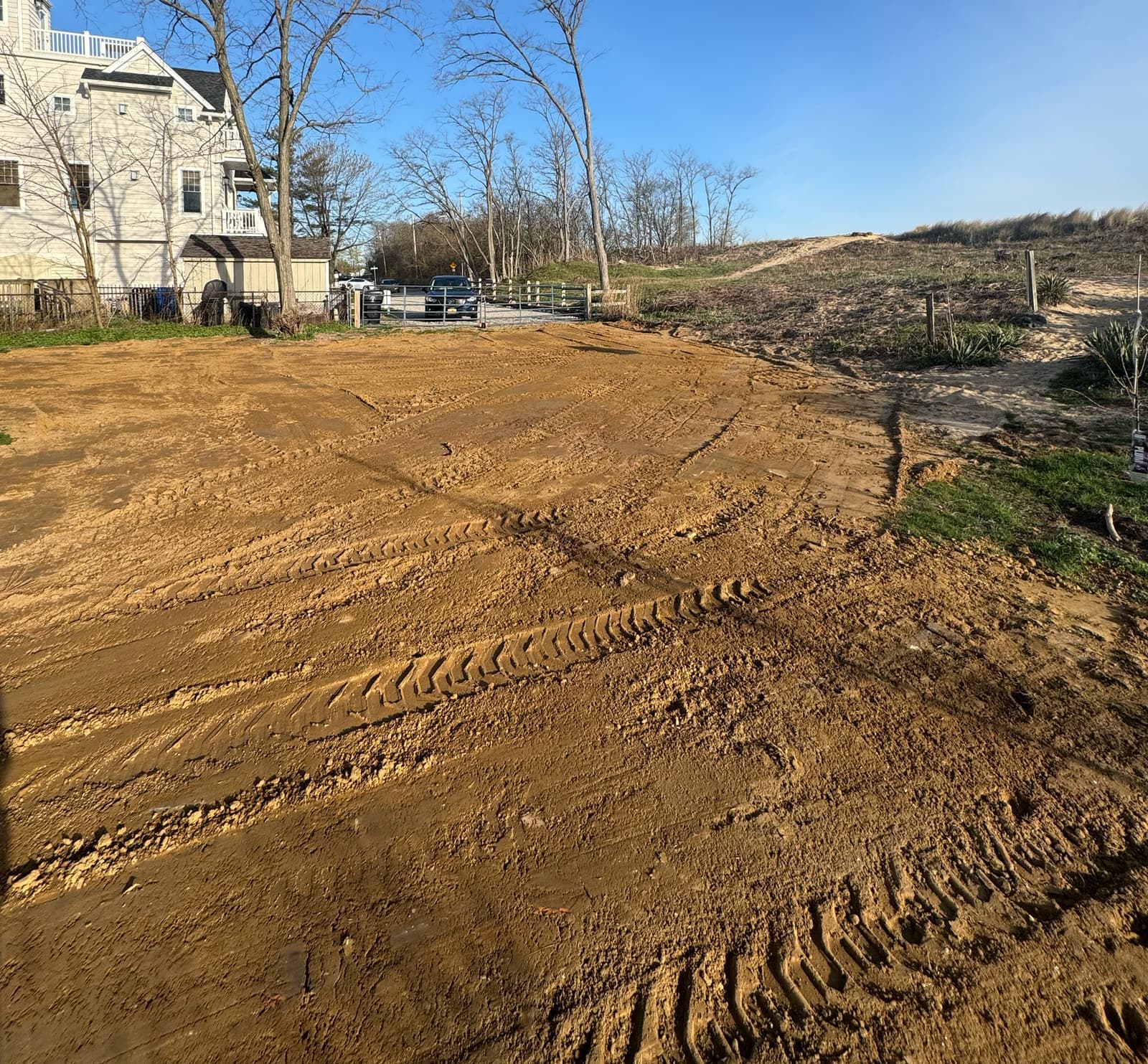 A cleared lot rough graded smooth beside a house, track marks still in the soil.