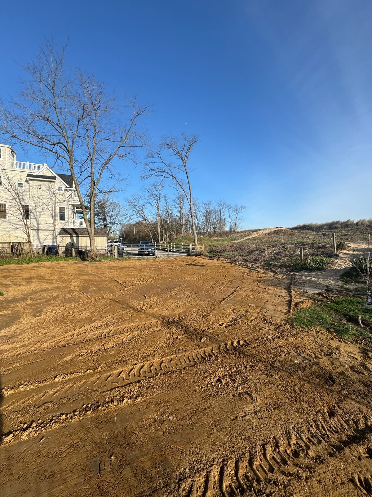 A cleared lot rough graded beside a house, track marks in the soil.