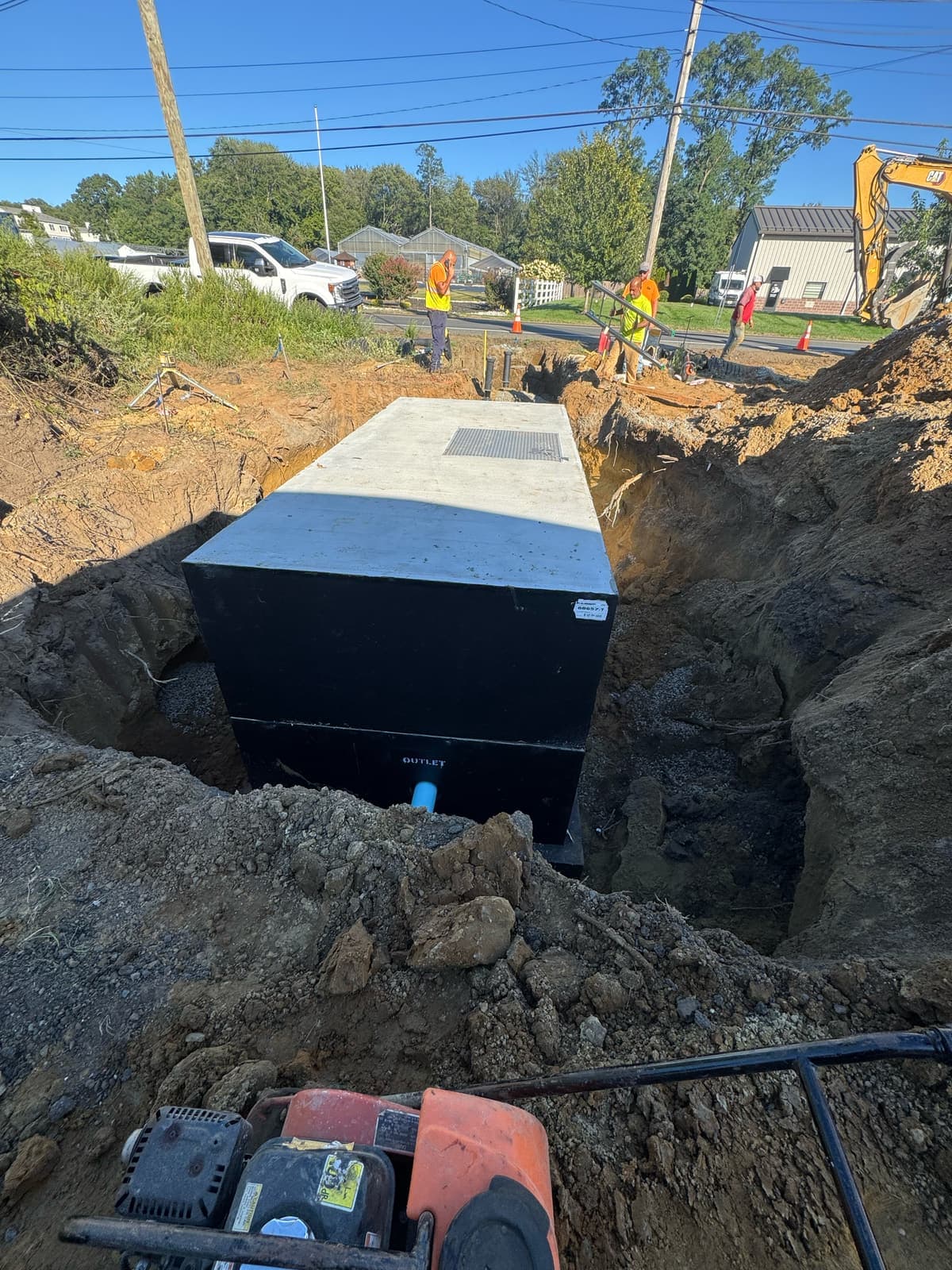 A precast concrete tank set into a deep excavation beside a residential street.